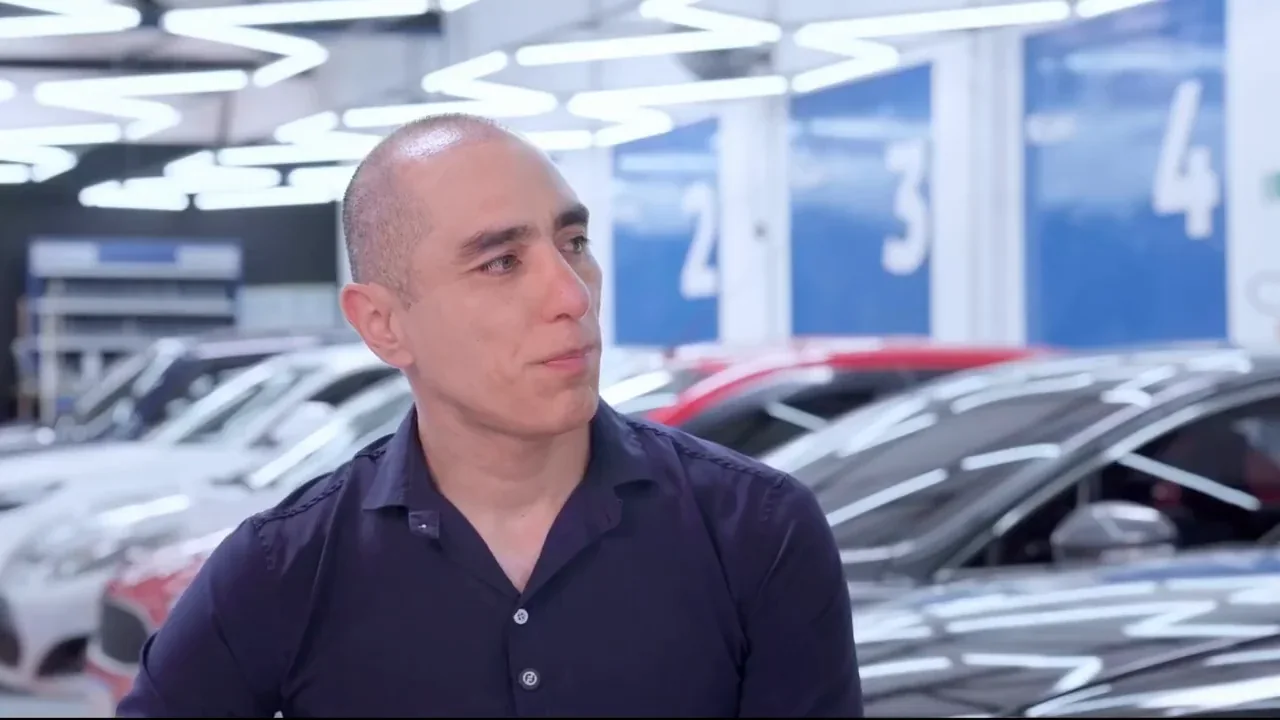 Rogério Ueta apresenta a Laav dentro da unidade, com os carros e a iluminação geométrica ao fundo.